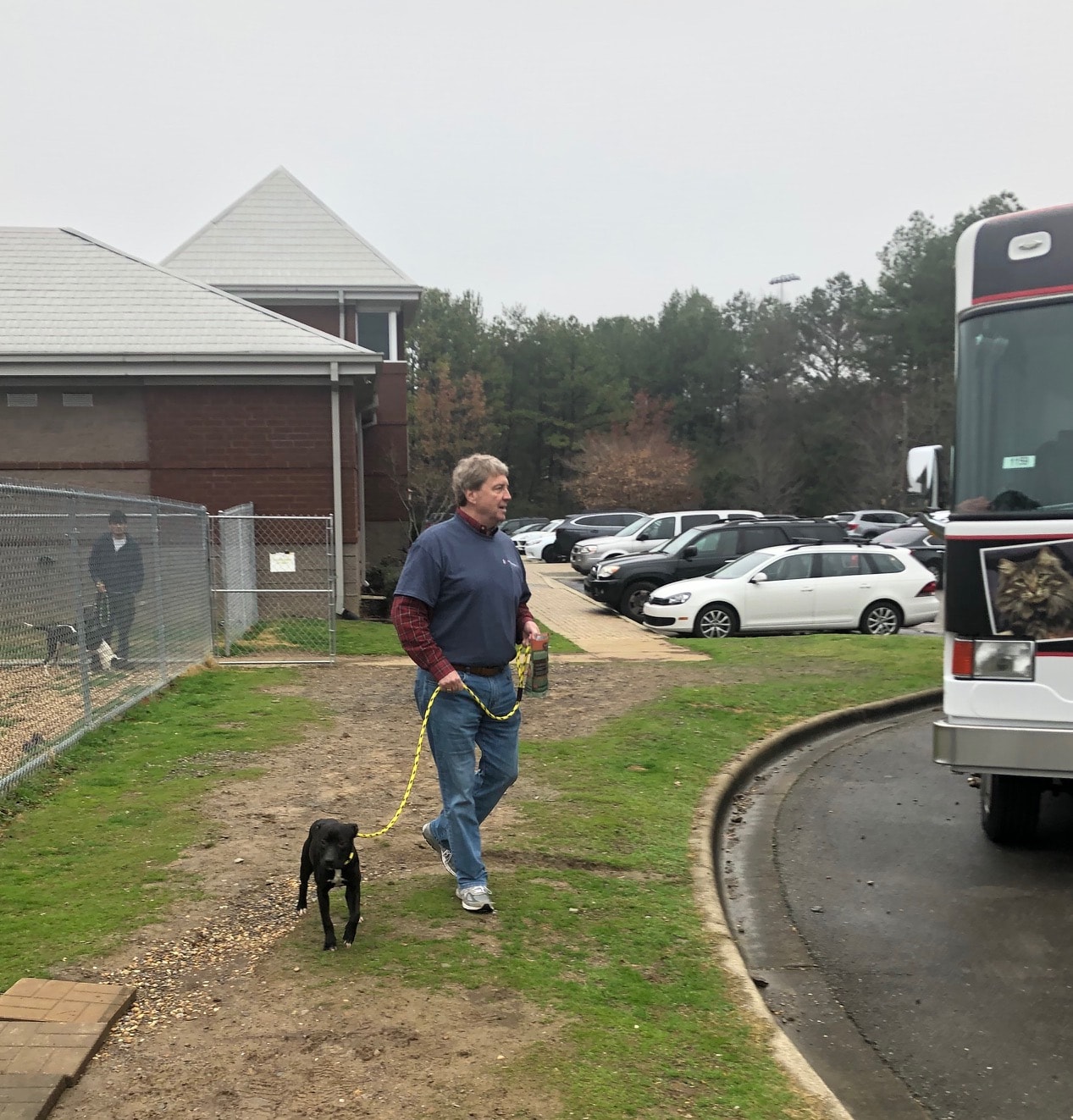 A Man Walking Down A Dirt Road In Front Of A Bus