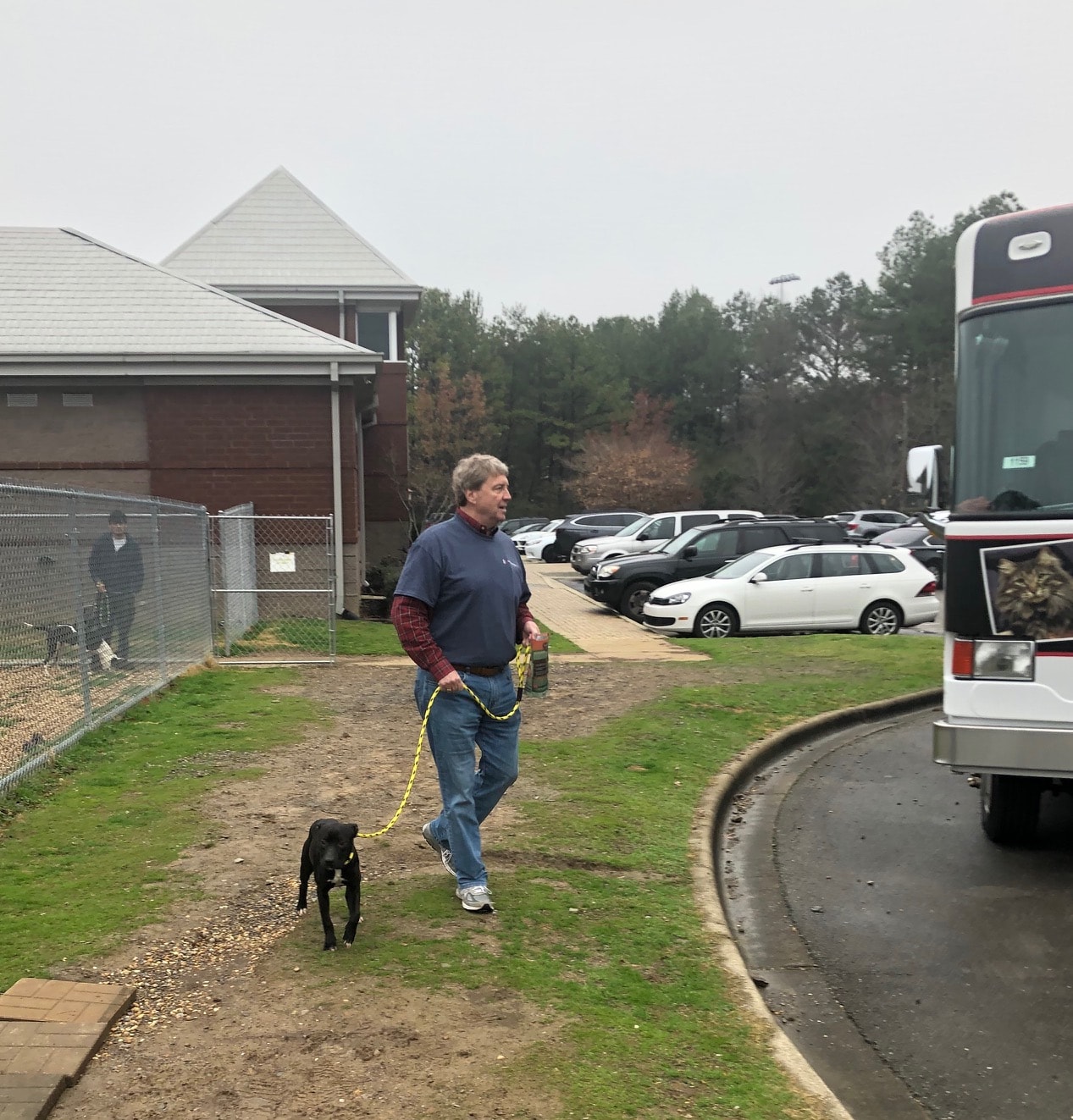 a man walking down a dirt road in front of a bus